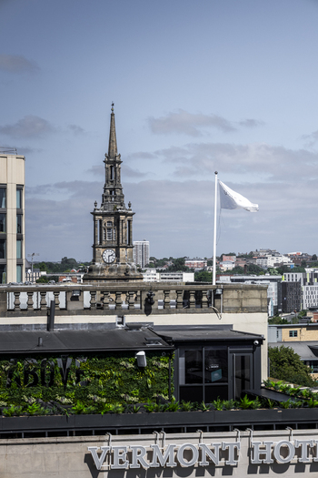 View of the historic church tower rising above the Vermont Hotel rooftop terrace with a green wall and a white flag in Newcastle upon Tyne England United Kingdom. View of the historic church tower rising above the Vermont Hotel rooftop terrace with a green wall and a white flag in Newcastle upon Tyne England United Kingdom.