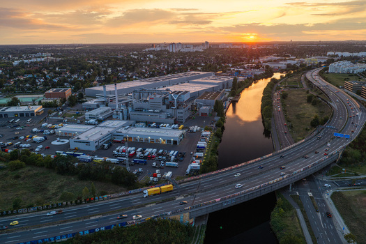 Aerial view of the BTB power plant facility situated along the canal with a highway bridge and urban landscape in the background during golden hour in Berlin Berlin Germany. Aerial view of the BTB power plant facility situated along the canal with a highway bridge and urban landscape in the background during golden hour in Berlin Berlin Germany.