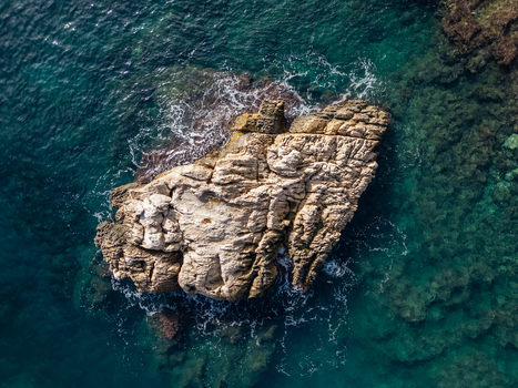 Aerial view of the rocky outcrop at Cala Llebeig surrounded by clear turquoise Mediterranean waters in El Poble Nou de Benitatxell Valencian Community Spain.