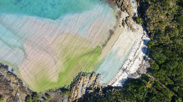 Aerial view of Chance Bay featuring vibrant turquoise and green water rugged rocky coastline and dense tropical vegetation in Whitsundays Queensland Australia. Aerial view of Chance Bay featuring vibrant turquoise and green water rugged rocky coastline and dense tropical vegetation in Whitsundays Queensland Australia.