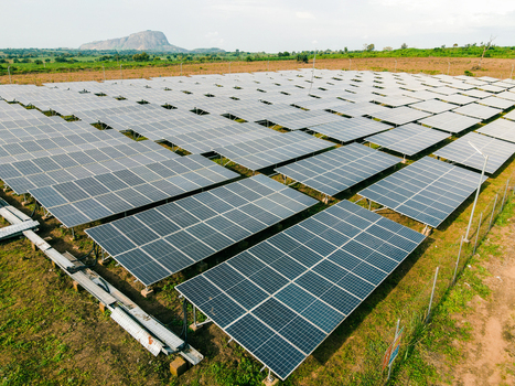 Aerial view of a large solar farm with rows of photovoltaic panels installed on grassy land featuring a prominent rocky hill in the background in Ogun State Nigeria.