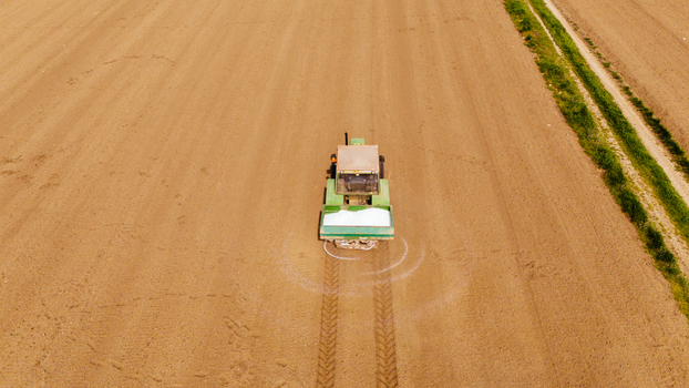 Aerial view of a green and beige tractor leaving white trails in a vast dry field near a verdant border Sremska Mitrovica Vojvodina Serbia. Aerial view of a green and beige tractor leaving white trails in a vast dry field near a verdant border Sremska Mitrovica Vojvodina Serbia.