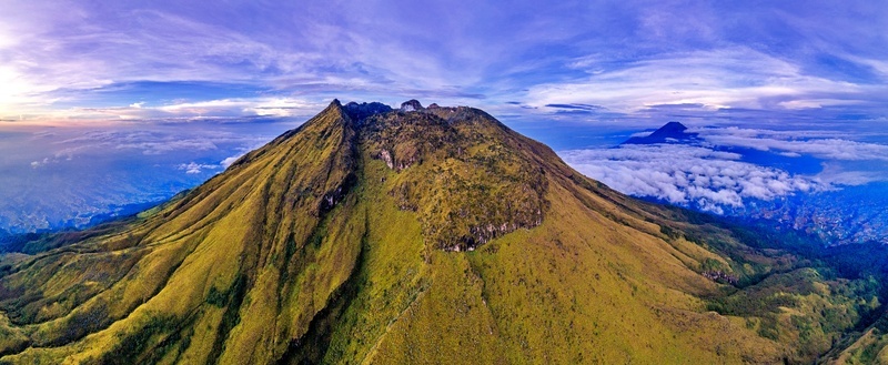 Aerial view of Mount Sumbing featuring rugged slopes and green vegetation under a dramatic sky with clouds Temanggung Central Java Indonesia. Aerial view of Mount Sumbing featuring rugged slopes and green vegetation under a dramatic sky with clouds Temanggung Central Java Indonesia.