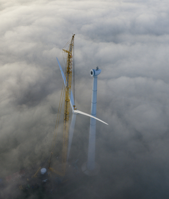 Aerial view of a wind turbine under construction with a tall yellow crane rising above a thick layer of white fog in Netherlands. Aerial view of a wind turbine under construction with a tall yellow crane rising above a thick layer of white fog in Netherlands.