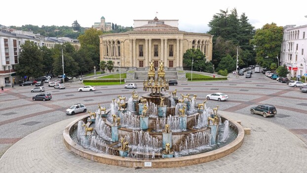 Kutaisi Georgia 18 September 2026 Aerial view of the Colchis Fountain in the city center surrounded by historic buildings trees and traffic on the square.