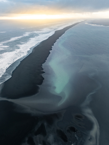 Aerial view of black sand beach with turquoise water and crashing waves under a golden sky in Iceland. Aerial view of black sand beach with turquoise water and crashing waves under a golden sky in Iceland.