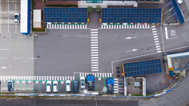 Aerial view of an electric vehicle charging station featuring solar panel carports parking spaces with parked cars and trucks and clear road markings in Milan Lombardy Italy.