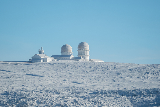View of a snow covered landscape under a clear blue sky with the observatory domes standing out against the horizon Covilh&atilde; Distrito da Guarda Portugal.