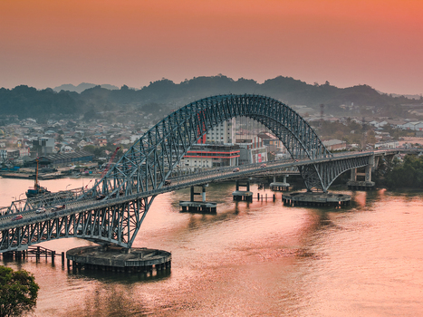 Aerial view of Jembatan Mahakam I spanning the Mahakam River with urban buildings and hills under a warm sunset sky in Kecamatan Samarinda Seberang Kalimantan Timur Indonesia. Aerial view of Jembatan Mahakam I spanning the Mahakam River with urban buildings and hills under a warm sunset sky in Kecamatan Samarinda Seberang Kalimantan Timur Indonesia.