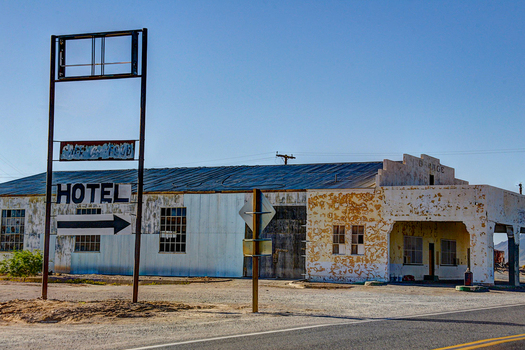 View of a weathered abandoned hotel and garage building with peeling paint and a vintage sign in the desert landscape of Death Valley California United States.