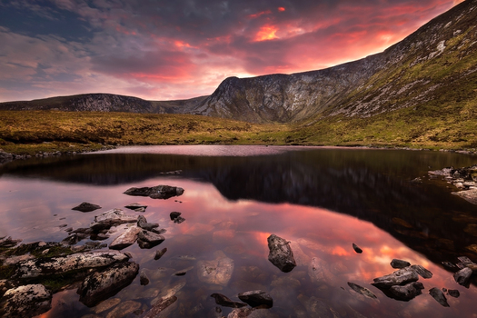 View of tranquil lake reflecting dramatic sunset clouds and rugged mountain cliffs with rocks in the foreground County Mayo Ireland. View of tranquil lake reflecting dramatic sunset clouds and rugged mountain cliffs with rocks in the foreground County Mayo Ireland.