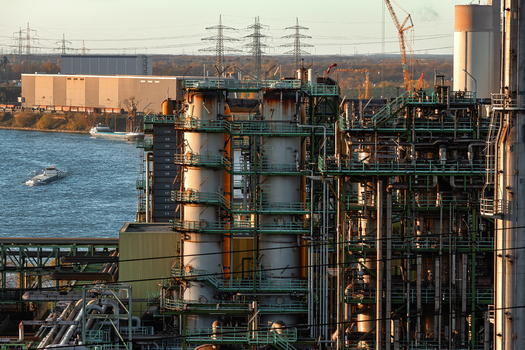 View of an industrial plant with steel towers and complex piping near a river with cargo ships at sunset in Duisburg North Rhine Westphalia Germany.