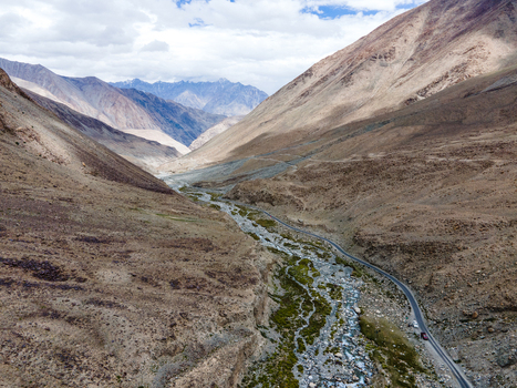 Aerial view of the rugged mountain valley in Ladakh with a winding road alongside a stream and sparse green vegetation in Ladakh Division Ladakh India. Aerial view of the rugged mountain valley in Ladakh with a winding road alongside a stream and sparse green vegetation in Ladakh Division Ladakh India.