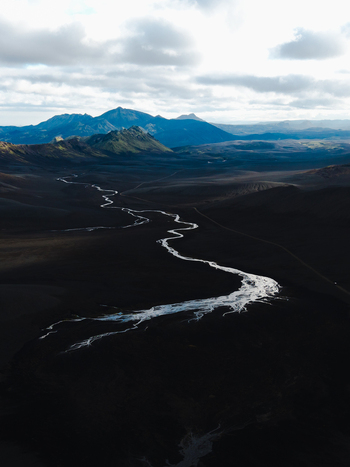 Aerial view of a silver river snakes through a dark rugged landscape under a cloudy sky Iceland. Aerial view of a silver river snakes through a dark rugged landscape under a cloudy sky Iceland.