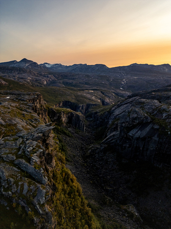 Aerial view of Hellemojuvet canyon with steep rocky cliffs and rugged mountainous terrain under a golden sunset sky in Hellmobotn Nordland Norway. Aerial view of Hellemojuvet canyon with steep rocky cliffs and rugged mountainous terrain under a golden sunset sky in Hellmobotn Nordland Norway.