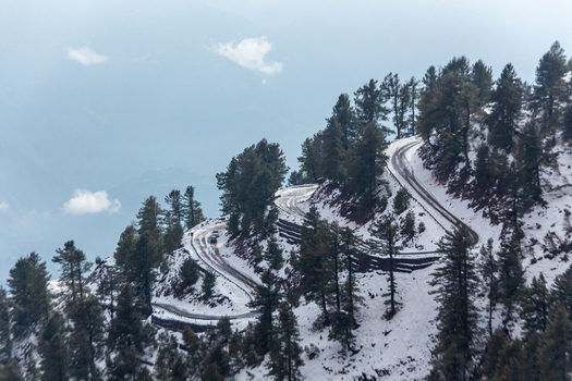 View of a winding road cutting through a snow dusted mountain embraced by towering pine trees under a soft sky Pir Chanasi Azad Kashmir Pakistan. View of a winding road cutting through a snow dusted mountain embraced by towering pine trees under a soft sky Pir Chanasi Azad Kashmir Pakistan.