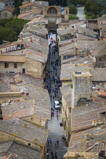 View of terracotta rooftops cascade down to a bustling street teeming with life in the medieval town San Gimignano Tuscany Italy. View of terracotta rooftops cascade down to a bustling street teeming with life in the medieval town San Gimignano Tuscany Italy.