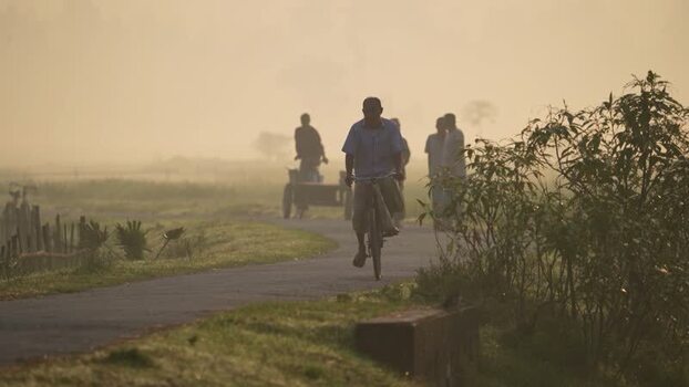 View of a man riding a bicycle on a misty rural road Bangladesh.