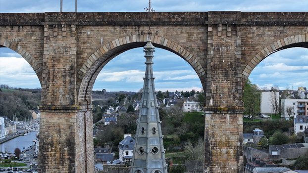 Aerial view of the spire of Eglise Saint Melaine framed by the stone arches of the Morlaix Viaduct with the town and harbor in the background Morlaix Bretagne France. Aerial view of the spire of Eglise Saint Melaine framed by the stone arches of the Morlaix Viaduct with the town and harbor in the background Morlaix Bretagne France.