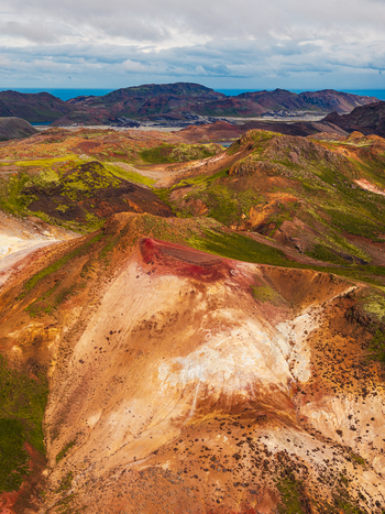 Aerial view of the rugged volcanic landscape featuring colorful mountains with patches of green moss and dark rocky terrain under a cloudy sky in Iceland. Aerial view of the rugged volcanic landscape featuring colorful mountains with patches of green moss and dark rocky terrain under a cloudy sky in Iceland.