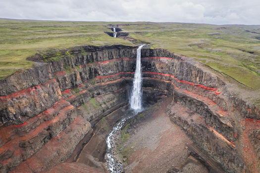Aerial view of Hengifoss waterfall cascading down basalt cliffs with distinct red clay layers under an overcast sky in Egilsstadir Fljotsdalshreppur Iceland. Aerial view of Hengifoss waterfall cascading down basalt cliffs with distinct red clay layers under an overcast sky in Egilsstadir Fljotsdalshreppur Iceland.