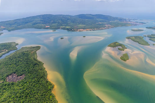 Aerial view of the winding Mesurado River estuary featuring intricate sandbars lush tropical forests and rolling green hills under a bright sky in Monrovia Montserrado Liberia.
