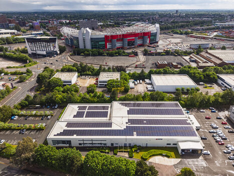 Aerial view of a large warehouse building with extensive solar panels on its roof with the Old Trafford stadium in the background in Stretford England United Kingdom.