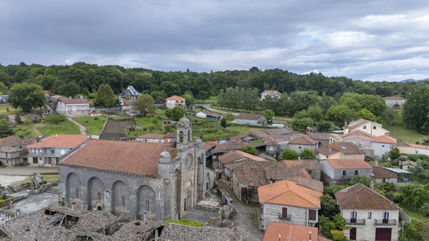 Aerial view of Iglesia de Santa Marina de Augas Santas surrounded by traditional stone houses and lush green forests under a cloudy sky Augas Santas Ourense Spain. Aerial view of Iglesia de Santa Marina de Augas Santas surrounded by traditional stone houses and lush green forests under a cloudy sky Augas Santas Ourense Spain.