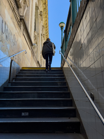 New York United States 14 May 2026 View of a person walking up the stairs of a subway entrance with tiled walls and a historic building facade under a blue sky. New York United States 14 May 2026 View of a person walking up the stairs of a subway entrance with tiled walls and a historic building facade under a blue sky.