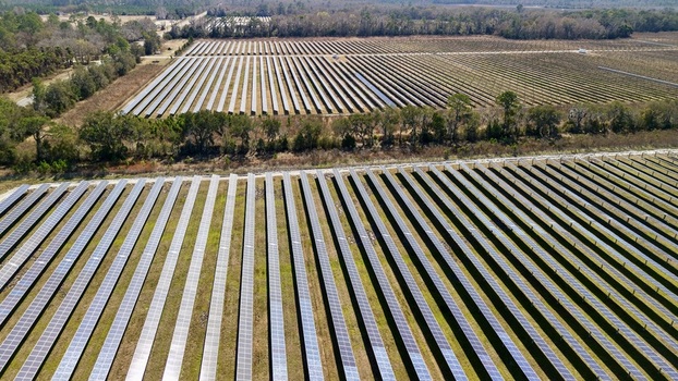 Aerial view of solar panels stretching across the landscape reflecting the sky s hue contrasting with the surrounding green fields Elkton Florida United States. Aerial view of solar panels stretching across the landscape reflecting the sky s hue contrasting with the surrounding green fields Elkton Florida United States.
