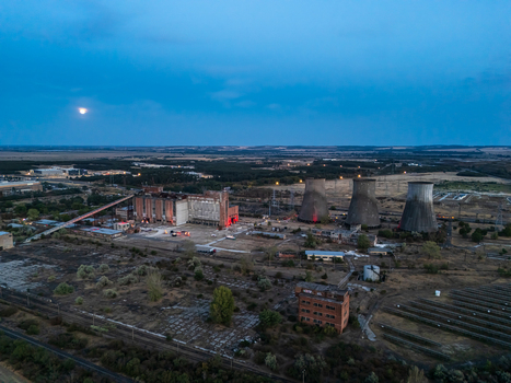 Aerial view of the closed Inota thermal power plant and its cooling towers at dusk with rail lines and illuminated industrial grounds in Inota Hungary.
