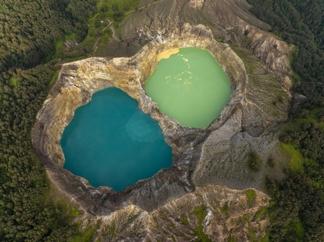 Aerial view of the Kelimutu National Park volcanic crater lakes with vibrant turquoise and green waters surrounded by rocky walls and forest in Detusoko East Nusa Tenggara Indonesia.
