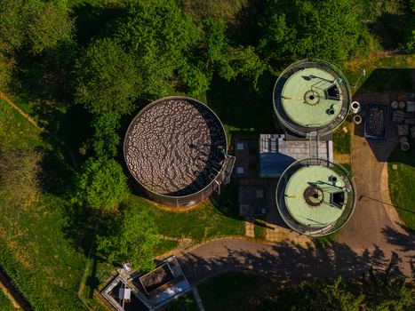 Aerial view of circular industrial tanks at a treatment plant surrounded by lush green trees and grass under bright sunlight in Kyjov South Moravian Region Czechia.