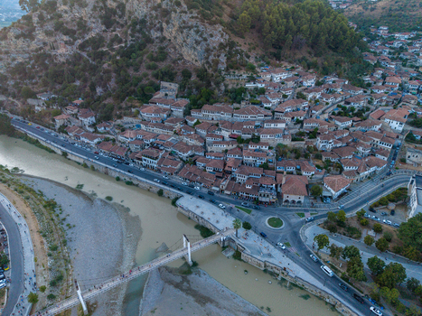 Aerial view of the historic town of Berat featuring traditional white houses with terracotta rooftops and a pedestrian bridge over the Osum River in Berat Berat County Albania.