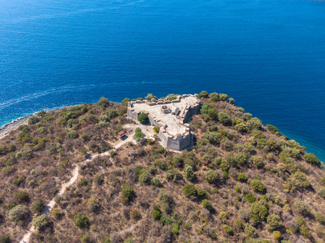 Aerial view of The Castle of Porto Palermo on a rocky peninsula surrounded by the blue Ionian Sea with Mediterranean vegetation and a dirt path Porto Palermo Qarku i Vlores Albania.