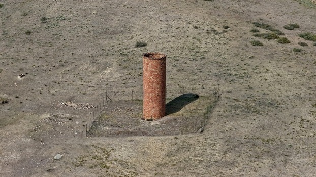 Aerial view of a historic brick chimney standing in a dry grassy field surrounded by a wire fence in Golden Colorado United States.