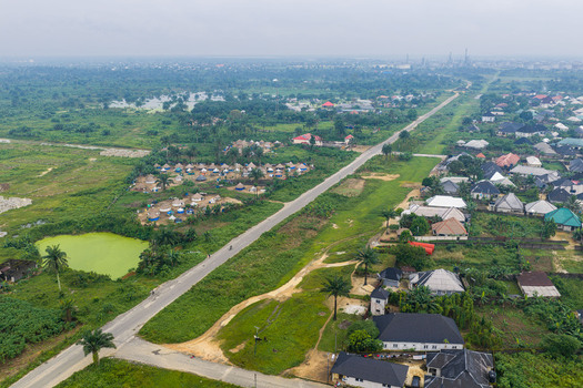 Aerial view of the outskirts of Port Harcourt featuring a long road residential houses a cluster of traditional round huts and a small green pond in Port Harcourt Rivers State Nigeria. Aerial view of the outskirts of Port Harcourt featuring a long road residential houses a cluster of traditional round huts and a small green pond in Port Harcourt Rivers State Nigeria.