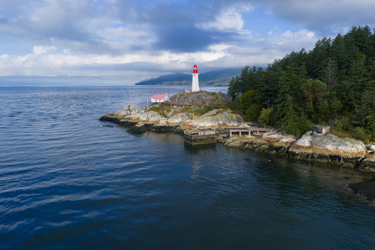Aerial view of Point Atkinson Lighthouse situated on a rocky headland surrounded by evergreen trees and the Pacific Ocean under a cloudy sky in West Vancouver British Columbia Canada.