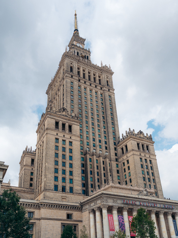 View of Palace of Culture and Science featuring its iconic spire intricate stone facade and classical architectural details under a cloudy sky in Warsaw Masovian Voivodeship Poland. View of Palace of Culture and Science featuring its iconic spire intricate stone facade and classical architectural details under a cloudy sky in Warsaw Masovian Voivodeship Poland.