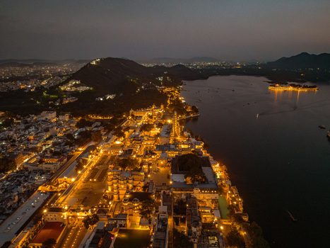 Aerial view of City Palace and Lake Pichola illuminated at night with historic architecture and glowing lights along the waterfront in Udaipur Rajasthan India.