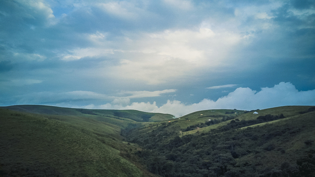 Aerial view of verdant rolling hills and a deep valley under a dramatic cloudy sky with hints of light breaking through Obudu Cross River Nigeria.