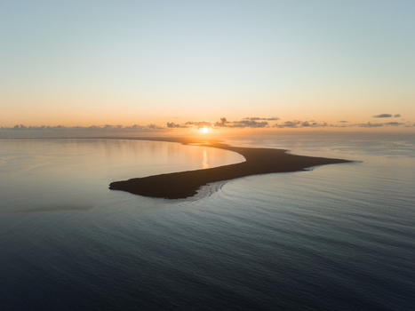 Aerial view of the sun rising over the tip of a long thin island surrounded by calm dark blue waters Ouvéa New Caledonia. Aerial view of the sun rising over the tip of a long thin island surrounded by calm dark blue waters Ouvéa New Caledonia.