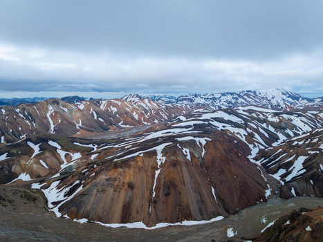 Aerial view of Landmannalaugar featuring colorful rhyolite mountains with snow patches and a river valley in Rangarthing ytra Iceland. Aerial view of Landmannalaugar featuring colorful rhyolite mountains with snow patches and a river valley in Rangarthing ytra Iceland.