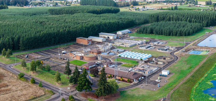 Aerial view of the wastewater treatment plant featuring circular sedimentation tanks processing buildings and surrounding fields in Woodburn Oregon United States. Aerial view of the wastewater treatment plant featuring circular sedimentation tanks processing buildings and surrounding fields in Woodburn Oregon United States.