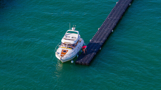Aerial view of a white motorboat moored at a floating dock with a person standing on the dock in West Bay England United Kingdom. Aerial view of a white motorboat moored at a floating dock with a person standing on the dock in West Bay England United Kingdom.