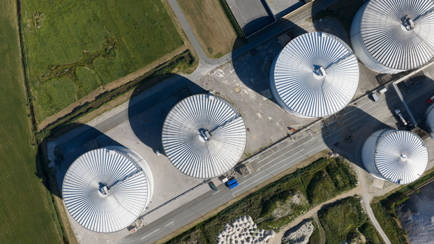 Aerial view of Cosun Beet Company featuring large industrial storage silos with metallic roofs surrounded by green fields and paved roads in Groningen Groningen Netherlands. Aerial view of Cosun Beet Company featuring large industrial storage silos with metallic roofs surrounded by green fields and paved roads in Groningen Groningen Netherlands.
