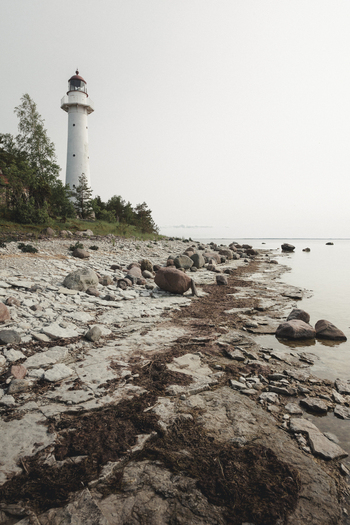 View of Saxby Lighthouse standing on a rocky coastline with seaweed and stones along the shore in Saxby Laane maakond Estonia.