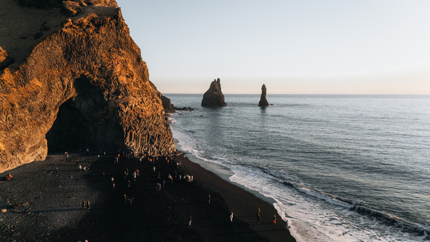 Aerial view of basalt cliffs embracing the dark sands of Reynisfjara Beach with the jagged Reynisdrangar sea stacks piercing the horizon Reynisfjara Beach Iceland.