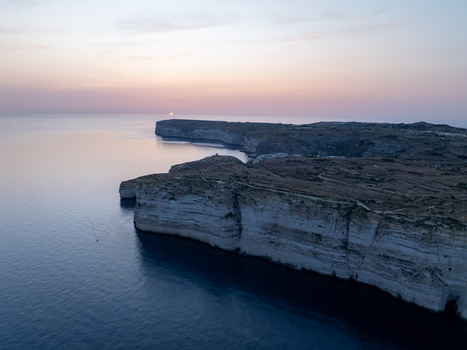 Aerial view of rugged cliffs meeting the tranquil sea under a soft pastel sky at Sanap Cliffs Munxar Gozo Malta. Aerial view of rugged cliffs meeting the tranquil sea under a soft pastel sky at Sanap Cliffs Munxar Gozo Malta.