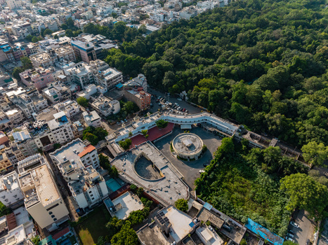 Aerial view of the circular building complex surrounded by dense urban rooftops and lush green parkland in Udaipur Rajasthan India.